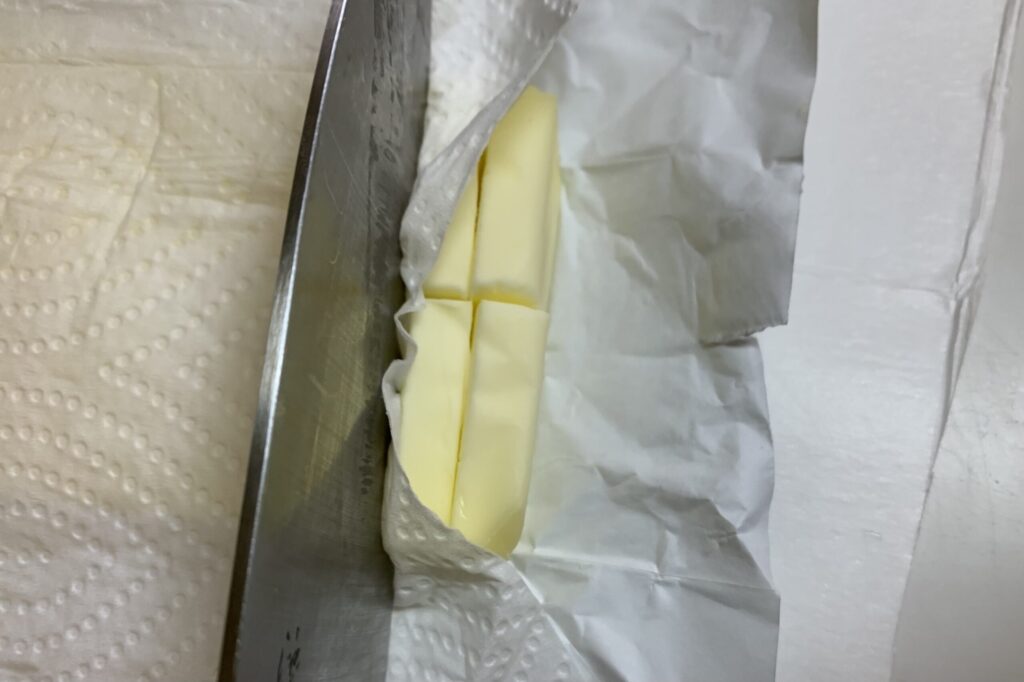 包丁が汚れないように、キッチンペーパーを挟んでバターをカットしている写真